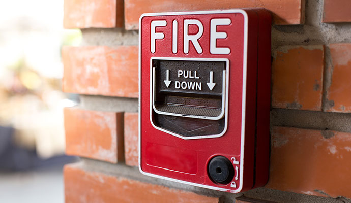 Red fire alarm pull station on brick wall