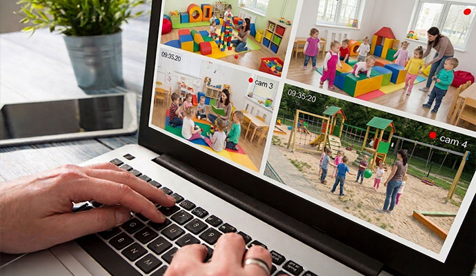 Laptop displaying multi-camera live video surveillance feed of daycare classrooms and playground
