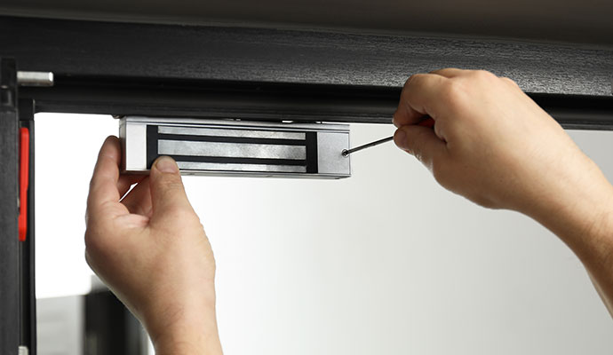 Technician hands using a screwdriver to install or repair a silver electromagnetic lock on a door frame