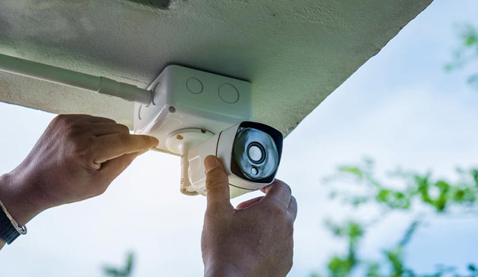 Technician installing a white security camera on a building