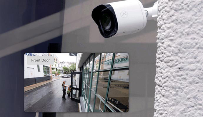 White outdoor bullet security camera with live front door video feed overlay