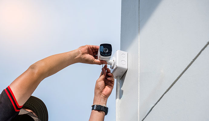 Technician installing a white outdoor bullet security camera on a wall