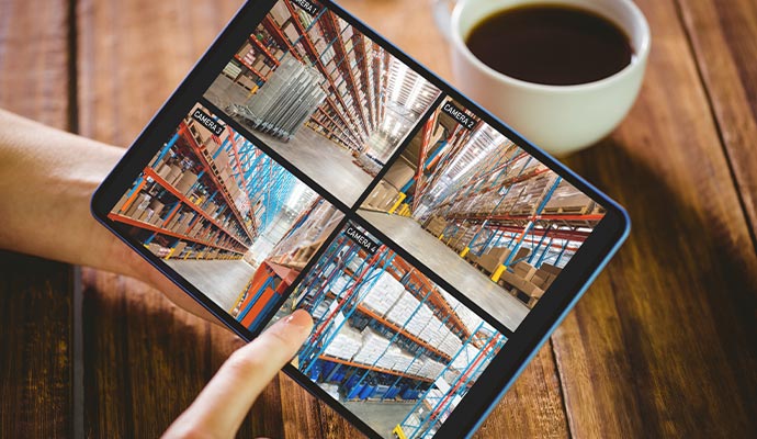 Person viewing four warehouse IP camera feeds on a tablet